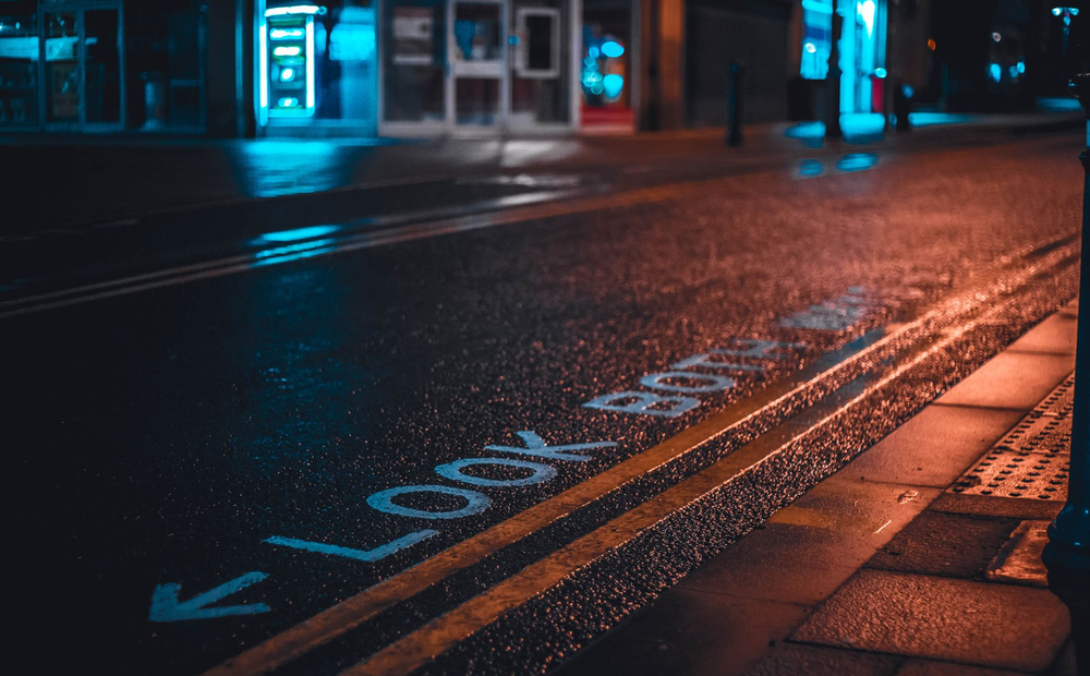 Night-time city street with lit bar frontages reflected in the water