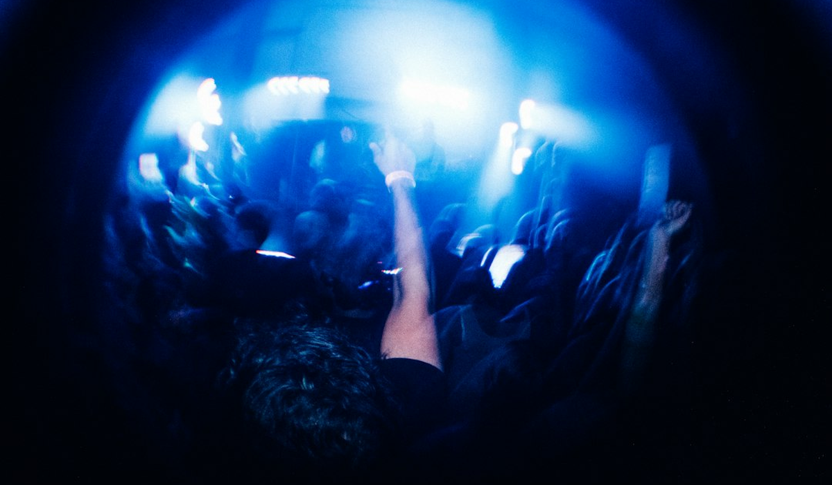 Busy venue floor lit by coloured beams with guests silhouetted in the haze