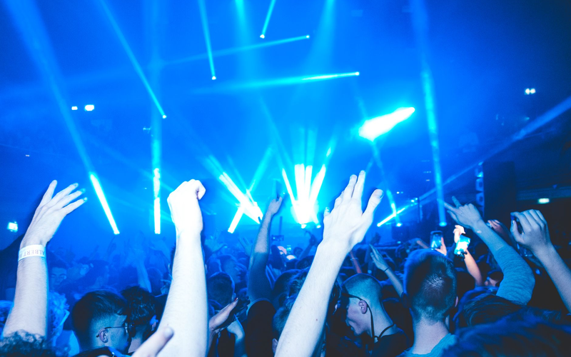 Wide view of a busy dance floor with laser beams and raised VIP booths