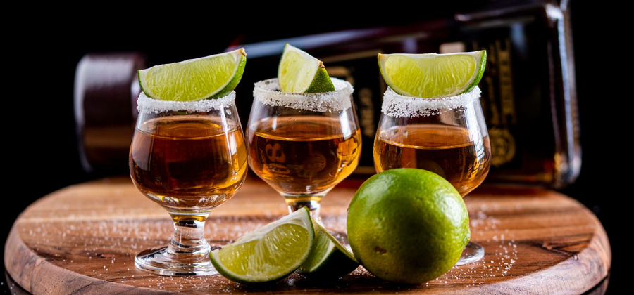 Row of filled shot glasses lined up on a board with salt and lime wedges